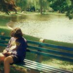 Niño escribiendo en un parque sentando junto a un río.