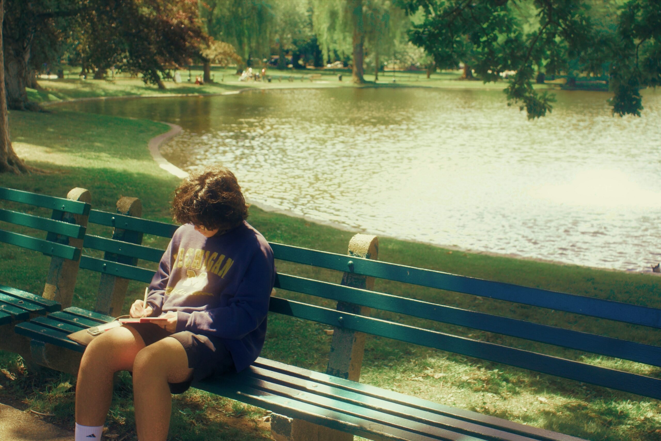 Niño escribiendo en un parque sentando junto a un río.